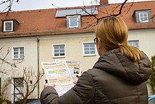 Frau schaut sich vor ihrem Haus einen Energieausweis an.